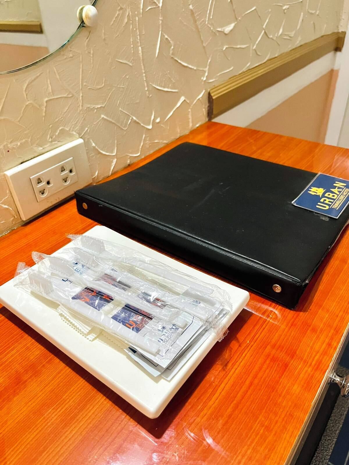 Una carpeta negra con etiqueta azul sobre una mesa de madera, junto a un plato blanco con objetos envueltos en plástico.