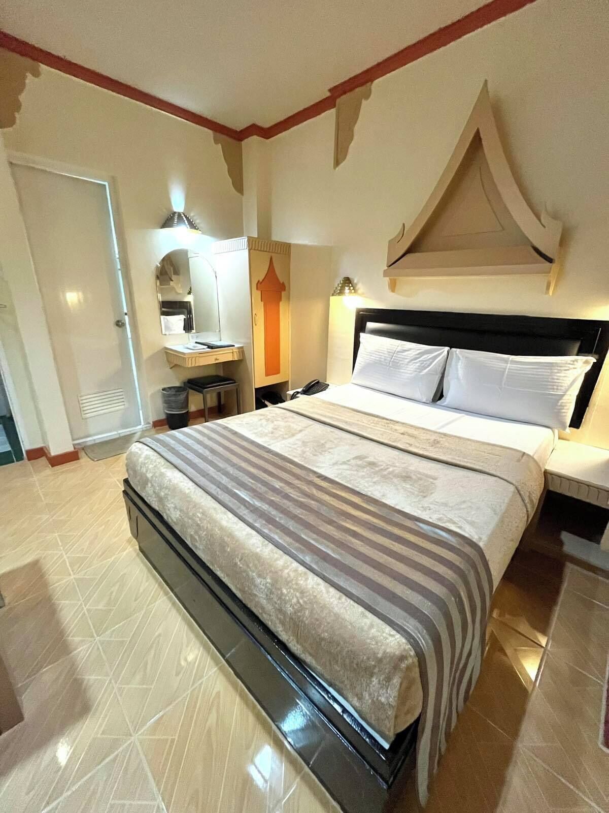 Ett hotellrum med en stor säng, ett sängbord, en byrå, en spegel, en garderob och ett badrum med toalett och handfat.