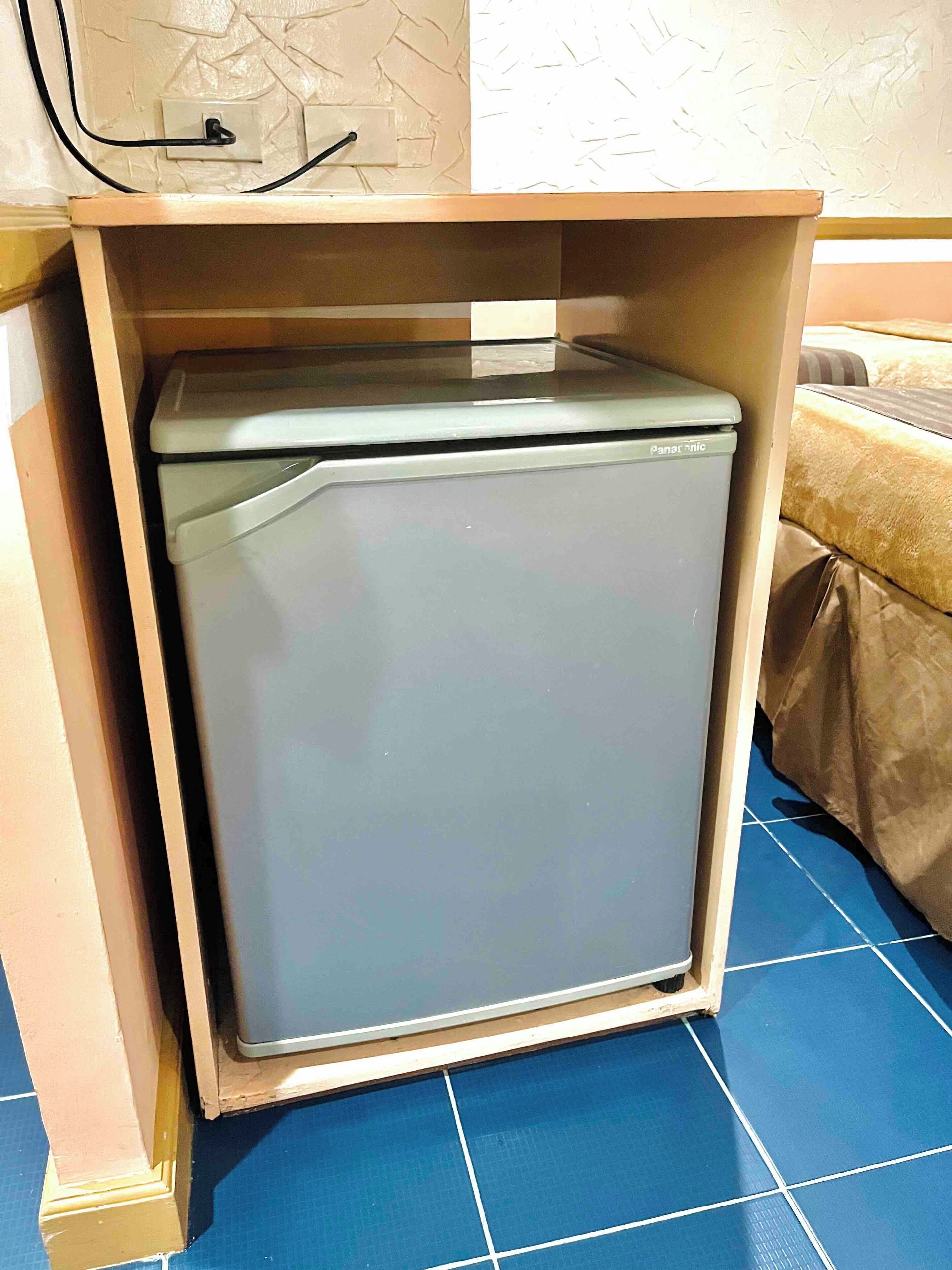 Un petit réfrigérateur dans une cuisine dont le sol est recouvert de carreaux bleus et le plan de travail est de couleur beige.