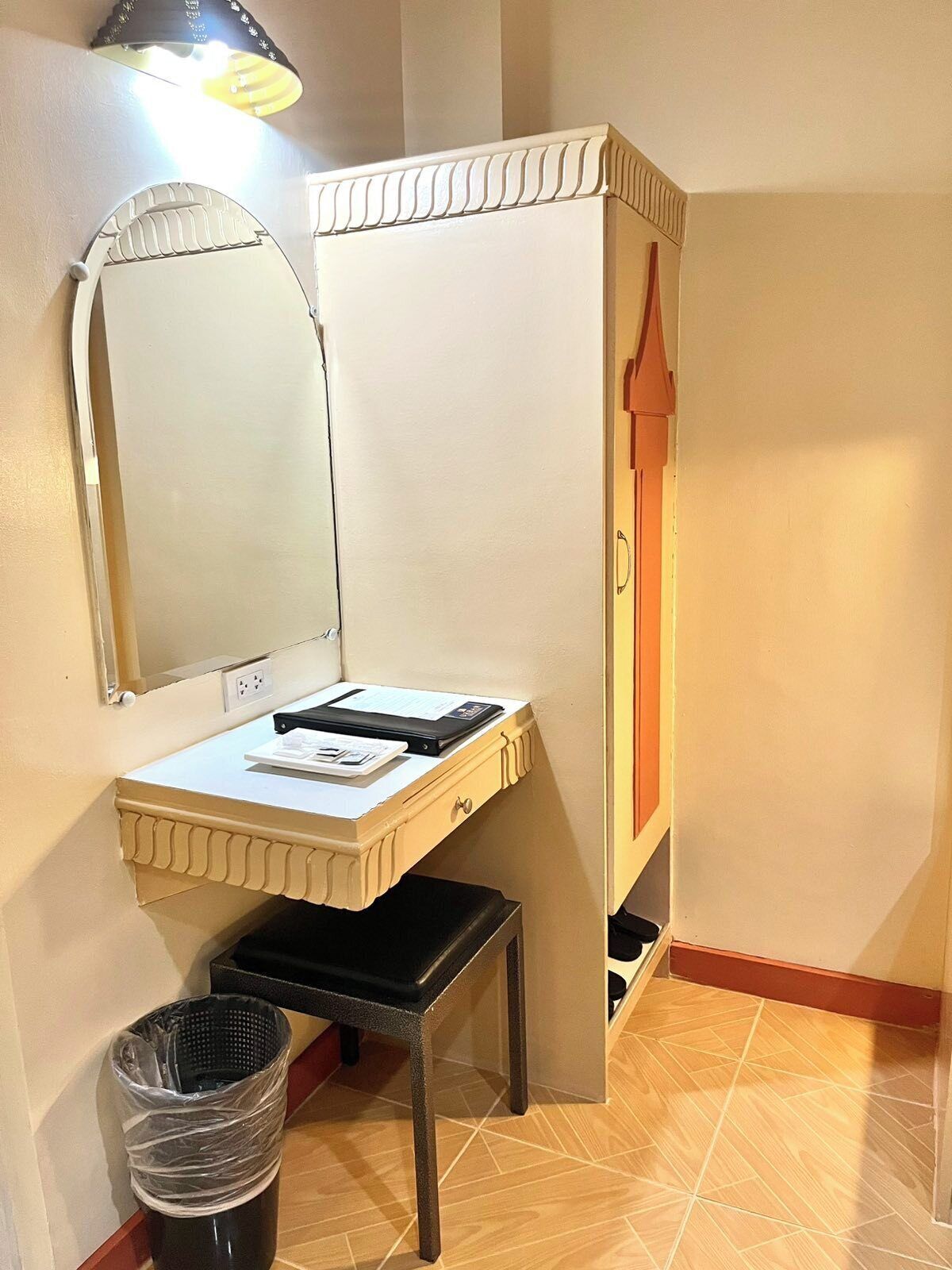A compact room with a white vanity, a mirror, a small stool, and a trash bin.