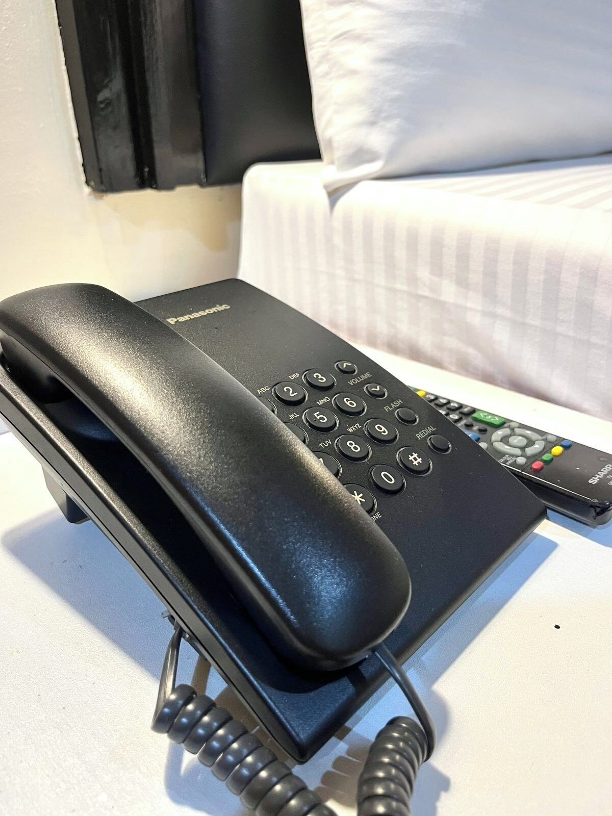 Musta hotellipuhelin ja kaukosäädin valkoisella alustalla.