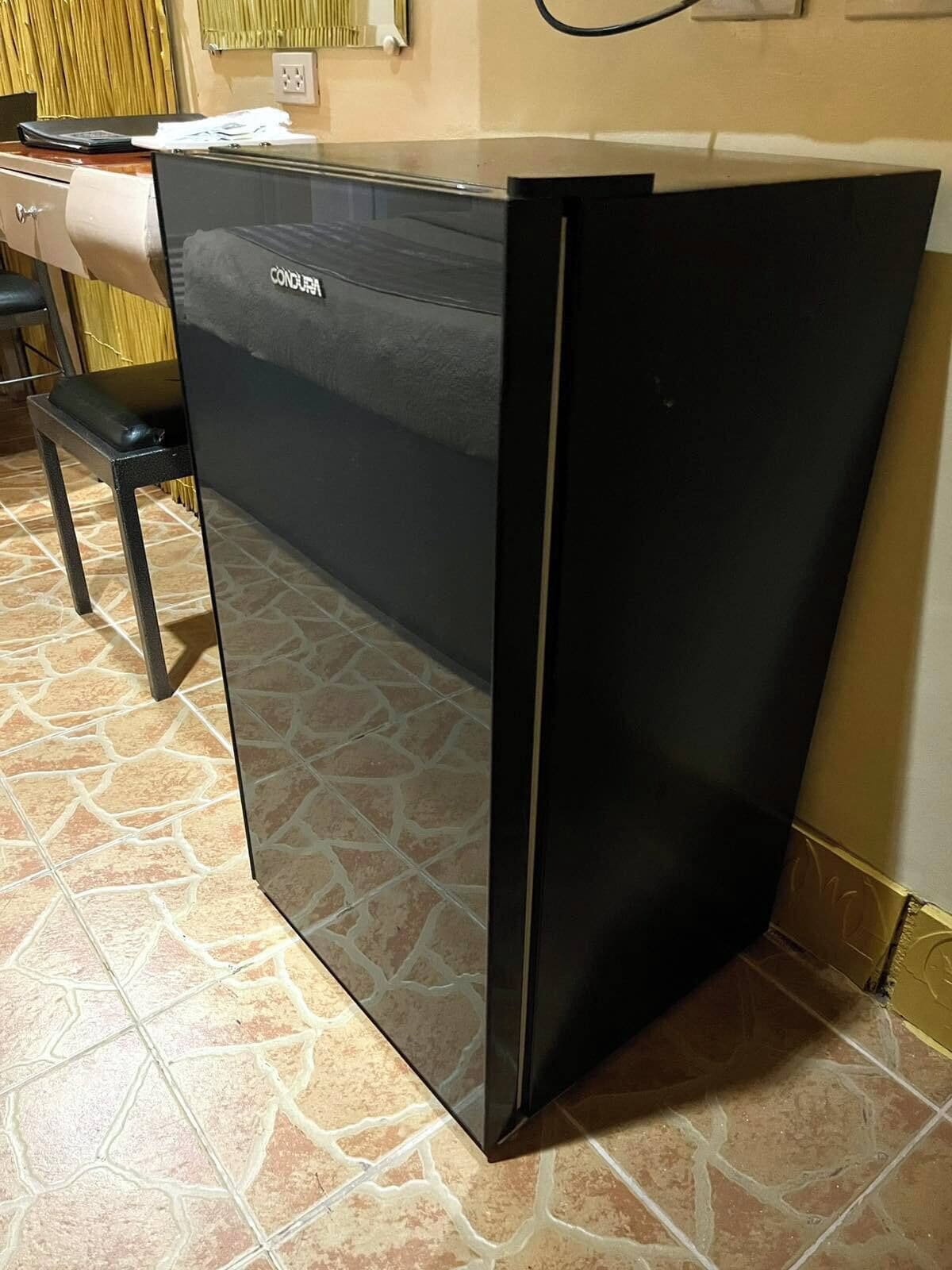 A black refrigerator in a kitchen with a tiled floor and a wooden cabinet to the left.