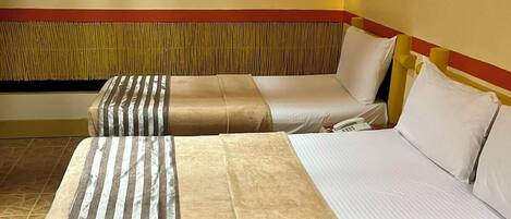 Ein Hotelzimmer mit zwei Betten, jeweils mit einer gestreiften Decke und weißen Kissen. Über den Betten hängt eine Wandleuchte.