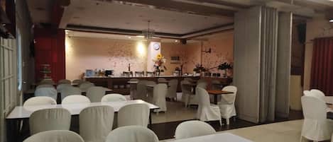 A restaurant with multiple tables and chairs, a bar area, and decorative elements like flowers and wall art.