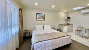 A hotel room with a bed, a desk, a chair, a small table, a sink, and a microwave. - Motel Hobson's Choice (Dargaville)