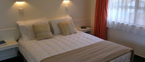 A neatly made bed with pillows, a bedside table with a book, and a wall-mounted light fixture.