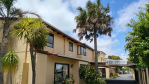 A building with a reception sign, multiple windows, and a variety of plants including palm trees. - Motel Hobson's Choice (Dargaville)