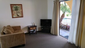 A living room with a sofa, a television on a stand, a small table with a lamp, and a large window with curtains. - Motel Hobson's Choice (Dargaville)