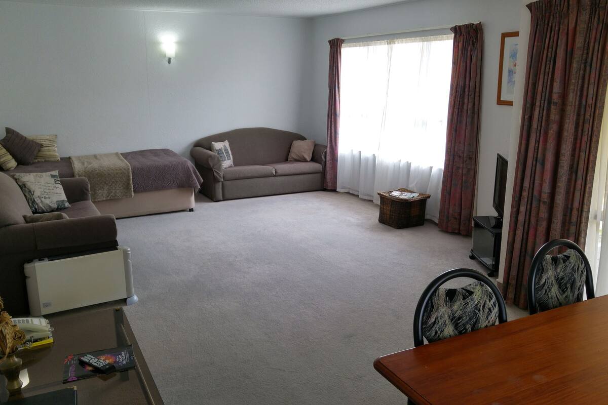 Uma sala de estar com sofá, mesa de centro, televisão e mesa de jantar.
