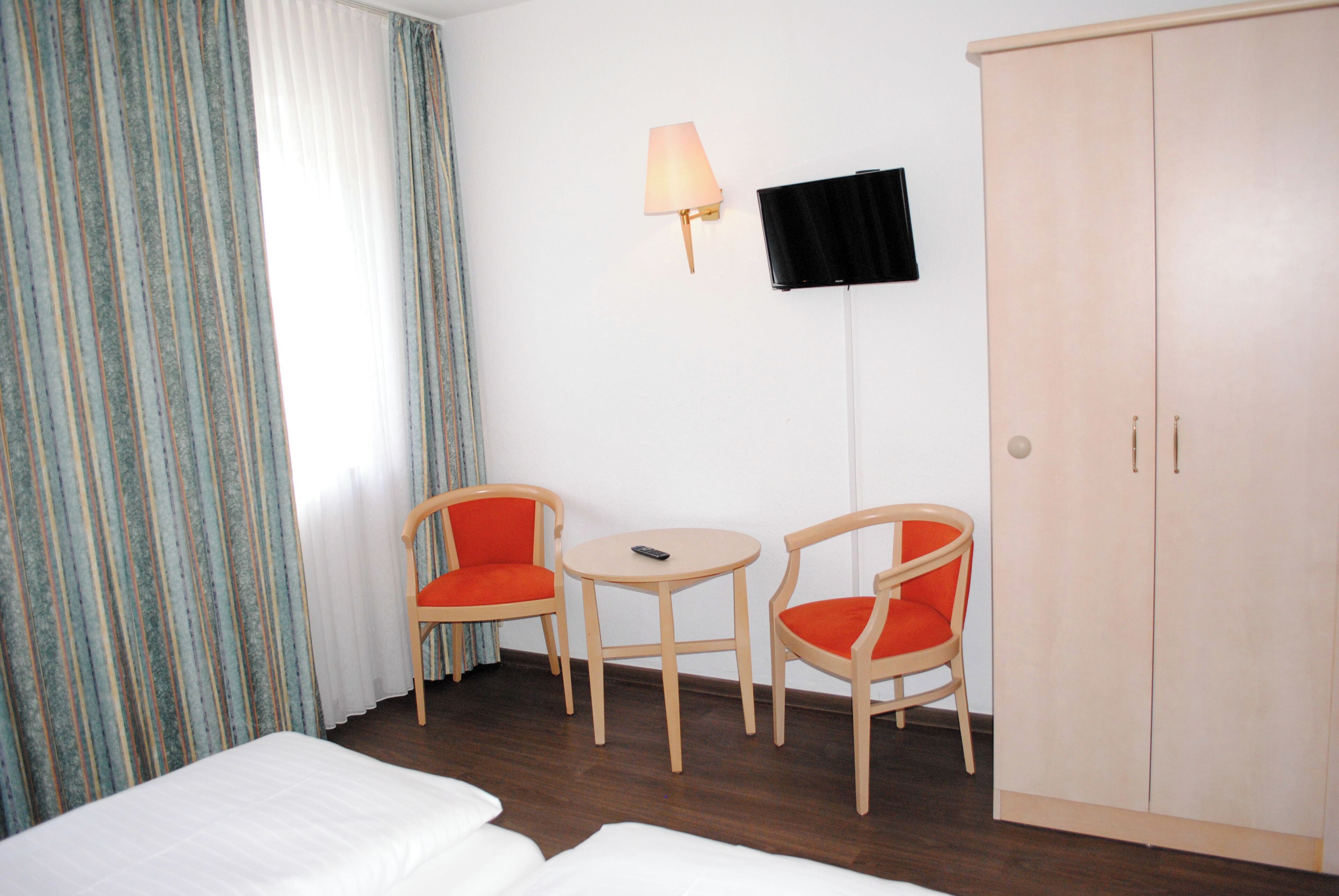 Ein Hotelzimmer mit einem Bett, zwei Stühlen, einem kleinen Tisch, einem Fernseher und einem Kleiderschrank.