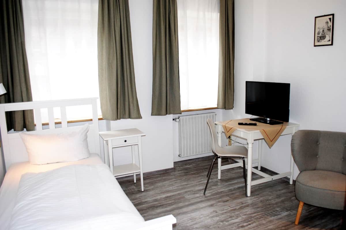 Habitación de hotel con cama, escritorio con silla, televisor y ventana con cortinas.