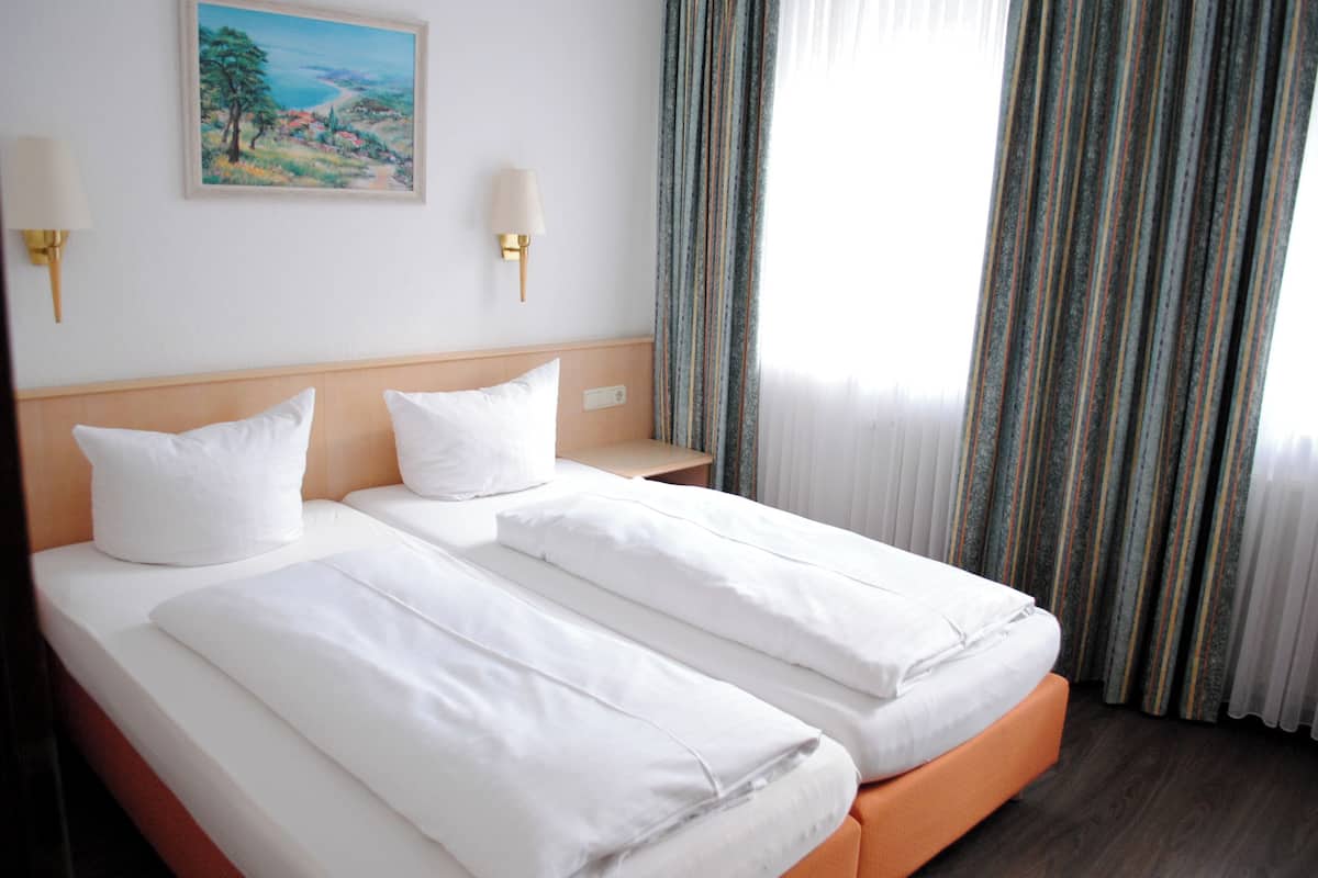 Habitación de hotel con dos camas, un cuadro en la pared y una ventana con cortinas.