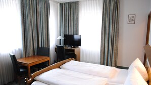 Habitació d'hotel amb un llit doble, un escriptori de fusta amb una cadira, una televisió i cortines.