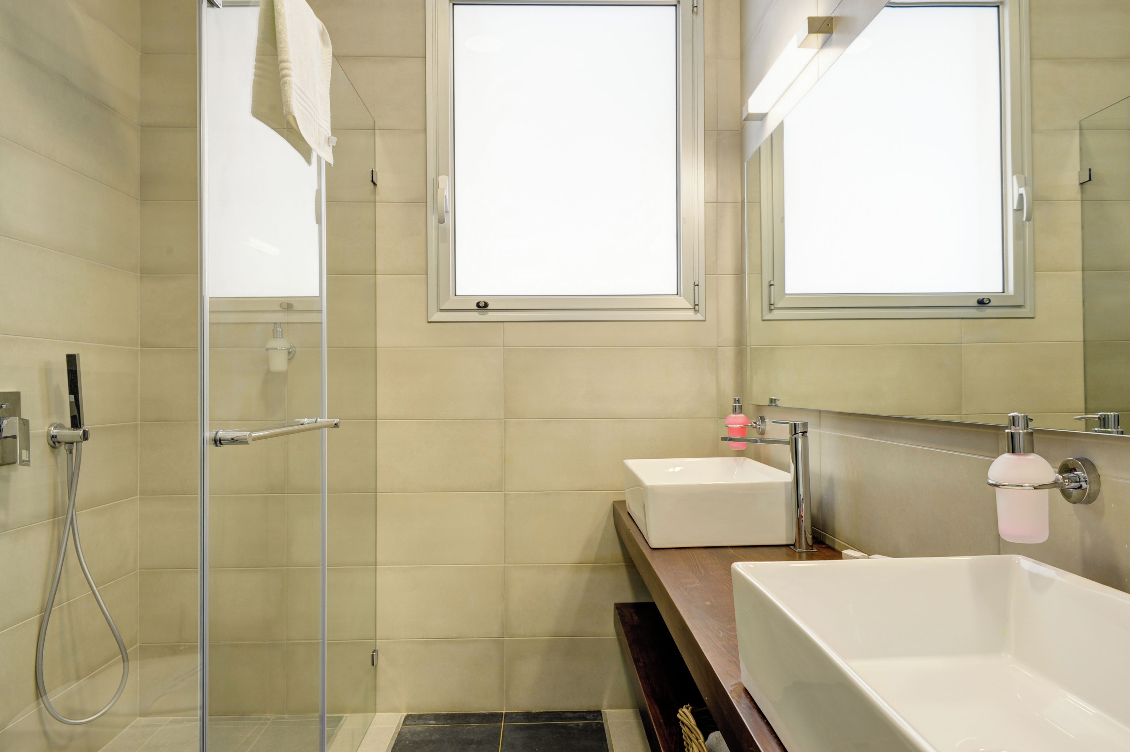 Une salle de bain moderne avec une douche à l’italienne en verre, un lavabo blanc, une grande baignoire et deux miroirs.