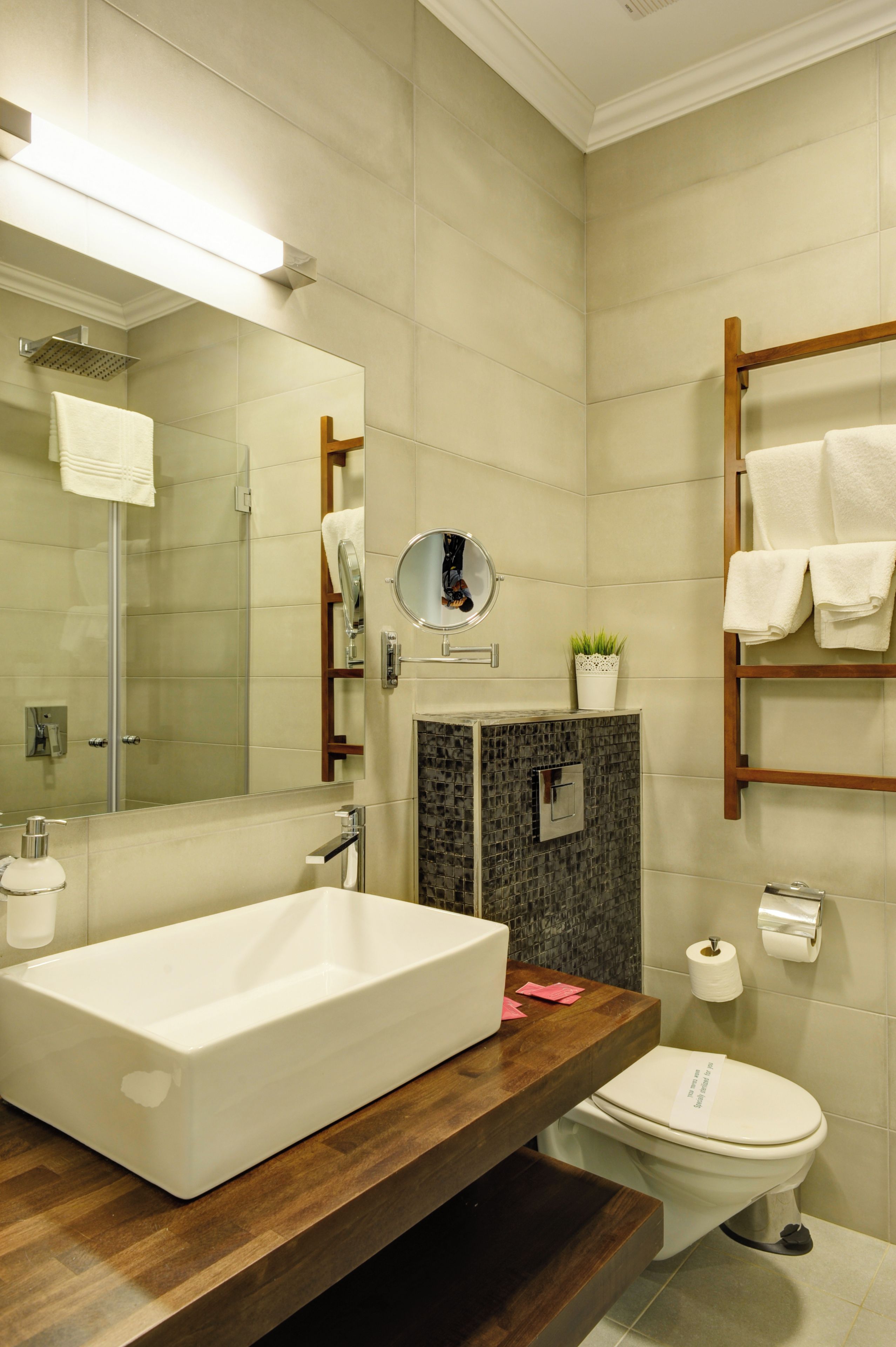 Une salle de bain moderne avec un grand miroir, un lavabo rectangulaire, des toilettes et un porte-serviettes en bois.