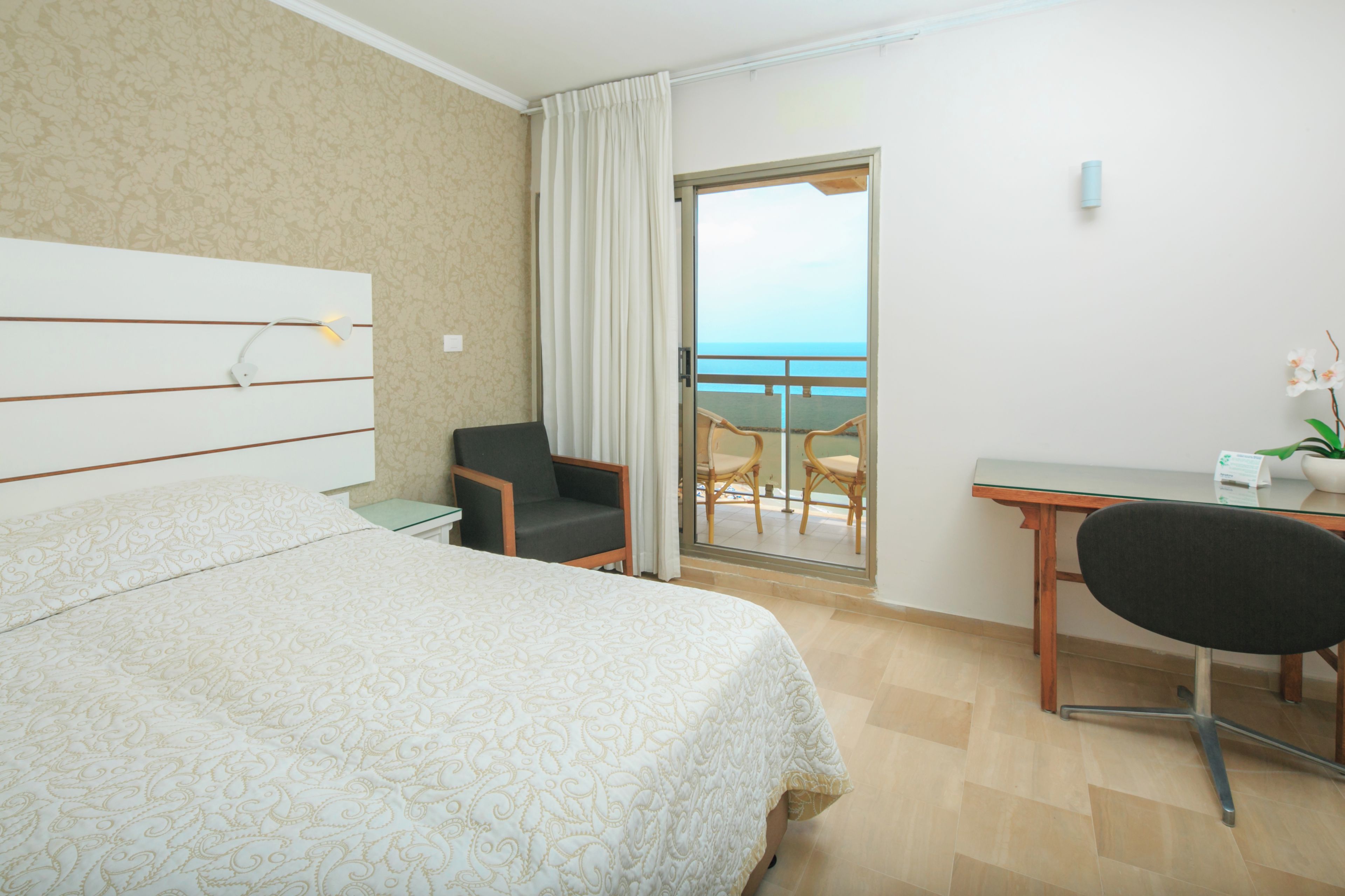 Ein Hotelzimmer mit Bett, Schreibtisch, Stuhl, einem kleinen Tisch und Meerblick.