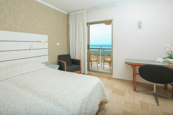 A hotel room with a bed, a desk, a chair, a small table, and a view of the ocean. - Residence Beach (Netanya)