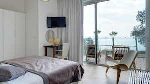 Un dormitorio con cama, televisor, escritorio con silla y balcón con vista al mar.