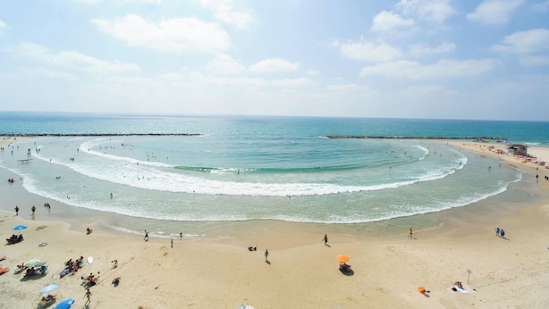 Una playa con una extensa zona arenosa, un rompeolas rocoso y un cielo despejado.