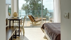 Un dormitorio con un amplio ventanal corredera que da a un balcón con vistas al mar y a árboles.