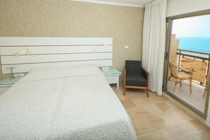 A hotel room with a large bed, a chair, a nightstand, and a balcony with a view of the beach. - Residence Beach (Netanya)