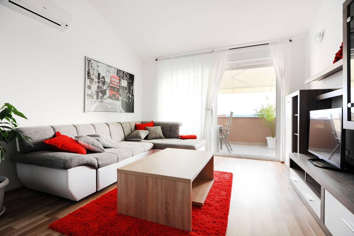 Un salon moderne avec un canapé gris, une table basse en bois et un tapis rouge.