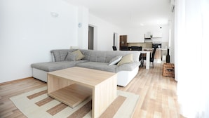 Ein modernes Wohnzimmer mit einer Eckcouch, einem Holztisch und einer Küche im Hintergrund.