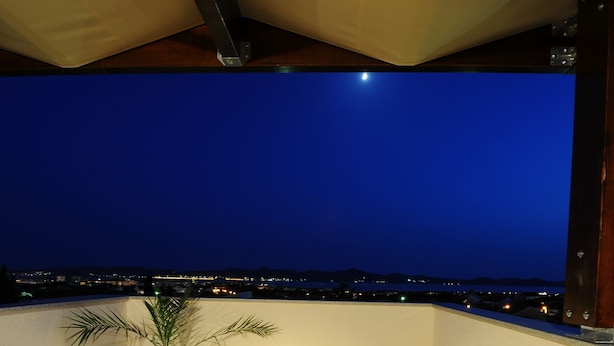 Eine Dachterrasse mit Tisch und Stühlen, einem Blumentopf und Blick auf die Stadt bei Nacht.