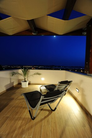 A rooftop terrace with a table and chairs, a potted plant, and a view of the city at night. - Apartments Hills (Zadar)