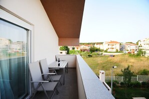 A balcony with a table and chairs, overlooking a residential area with houses and a grassy field. - Apartments Hills (Zadar)