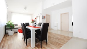 Ein moderner Essbereich mit einem weißen Tisch, schwarzen Stühlen und einer roten Tischmatte. Auf dem Boden steht ein Blumentopf und liegt ein roter Teppich. Die Wände sind weiß und der Boden aus Holz.