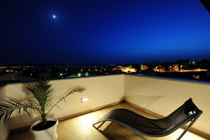 A balcony with a chair, a potted plant, and a view of a cityscape at night. - Apartments Hills (Zadar)