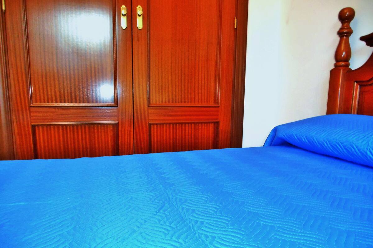 A room with a wooden wardrobe and a bed with a blue bedspread.