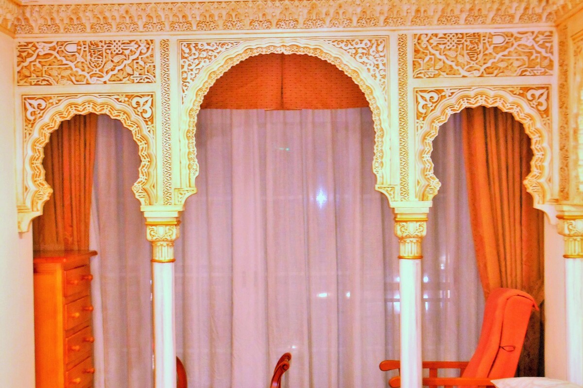 A room with ornate architectural details, a bed, two chairs, and a curtain.