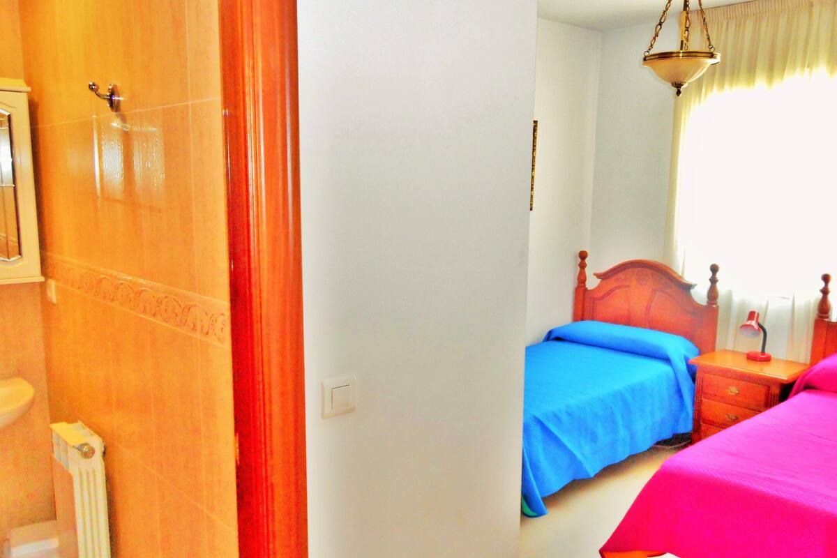 A bedroom with a wooden door, a radiator, a bedside table with a lamp, and a window with curtains.
