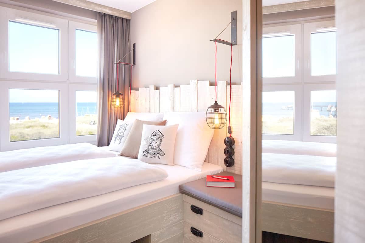 A hotel room with two beds, a view of the beach, and a bedside table with a book and lamp.