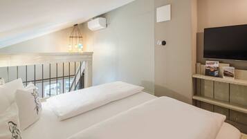 Habitación de hotel con una cama, televisor, estante con libros y balcón con barandilla.