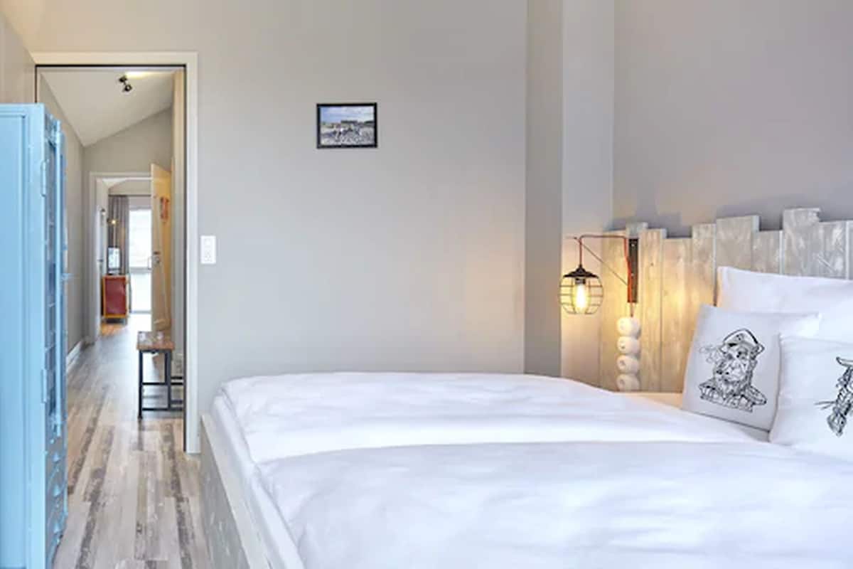 A bedroom with a large bed, a bedside table, a wall-mounted lamp, and a framed picture.