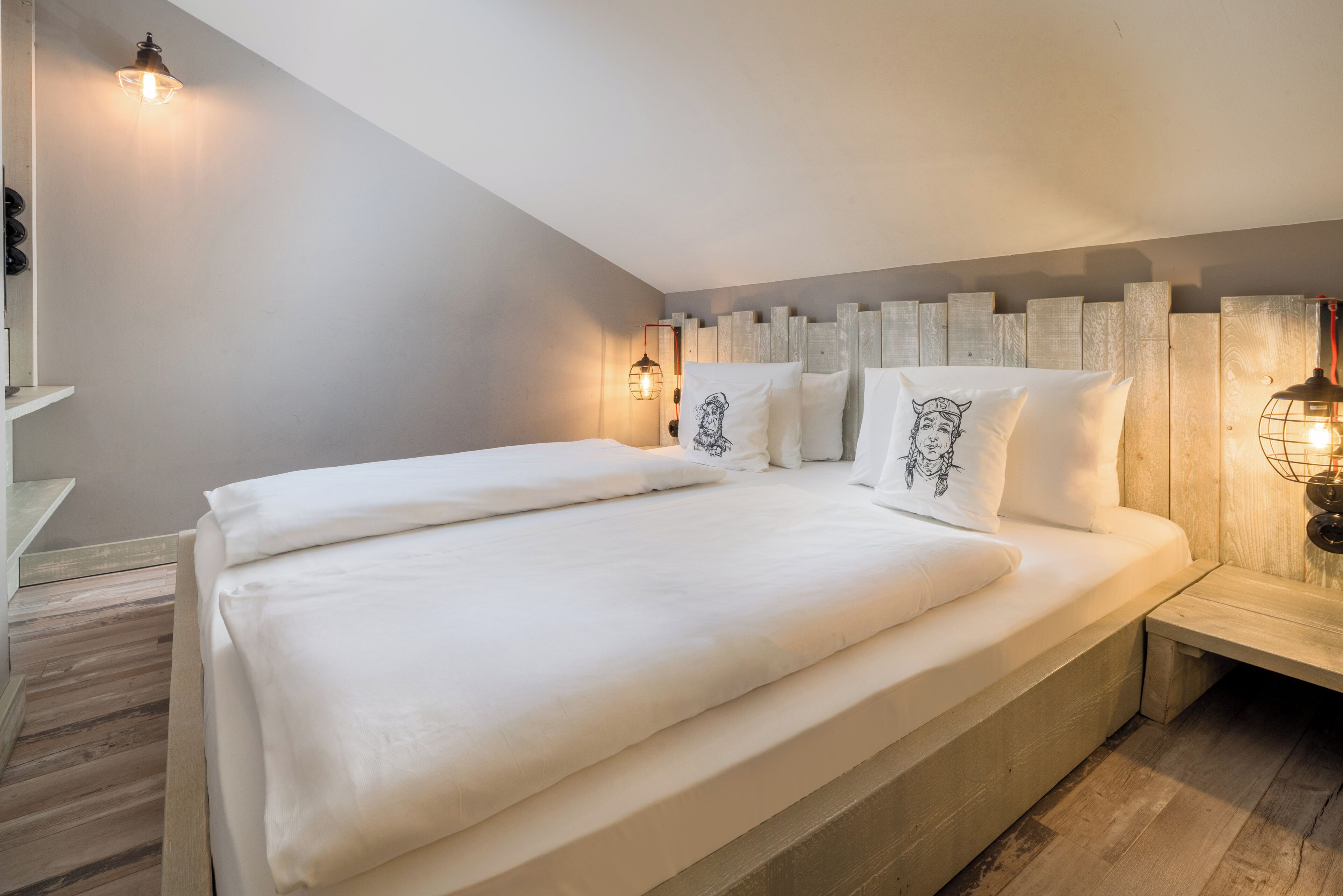 Un dormitorio con una cama grande, cabecera de madera, lámparas de noche y techo inclinado.
