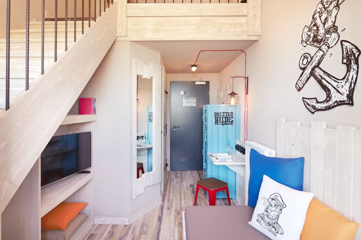 A modern interior with a staircase, a TV mounted on a wooden shelf, a desk with a chair, and a wall with a graphic.