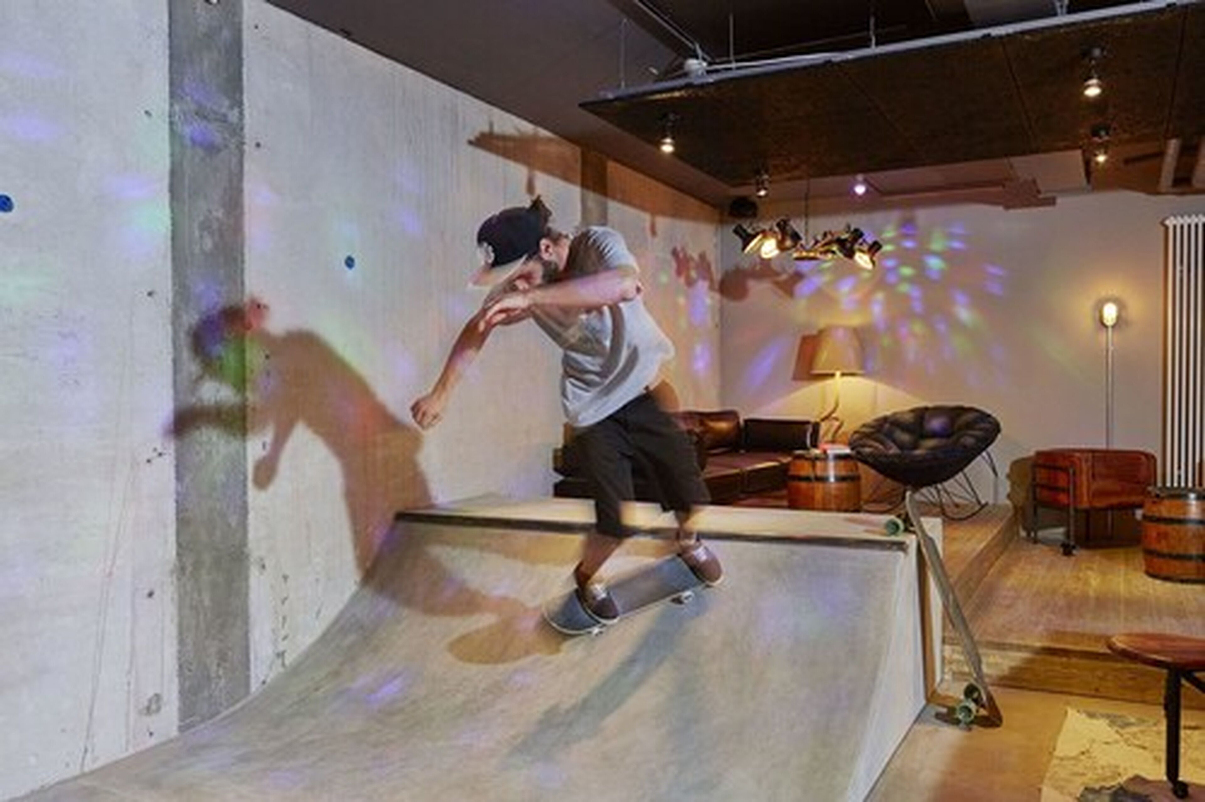 A person skateboarding in a room with a ramp, wooden furniture, and a projector casting light patterns on the wall.