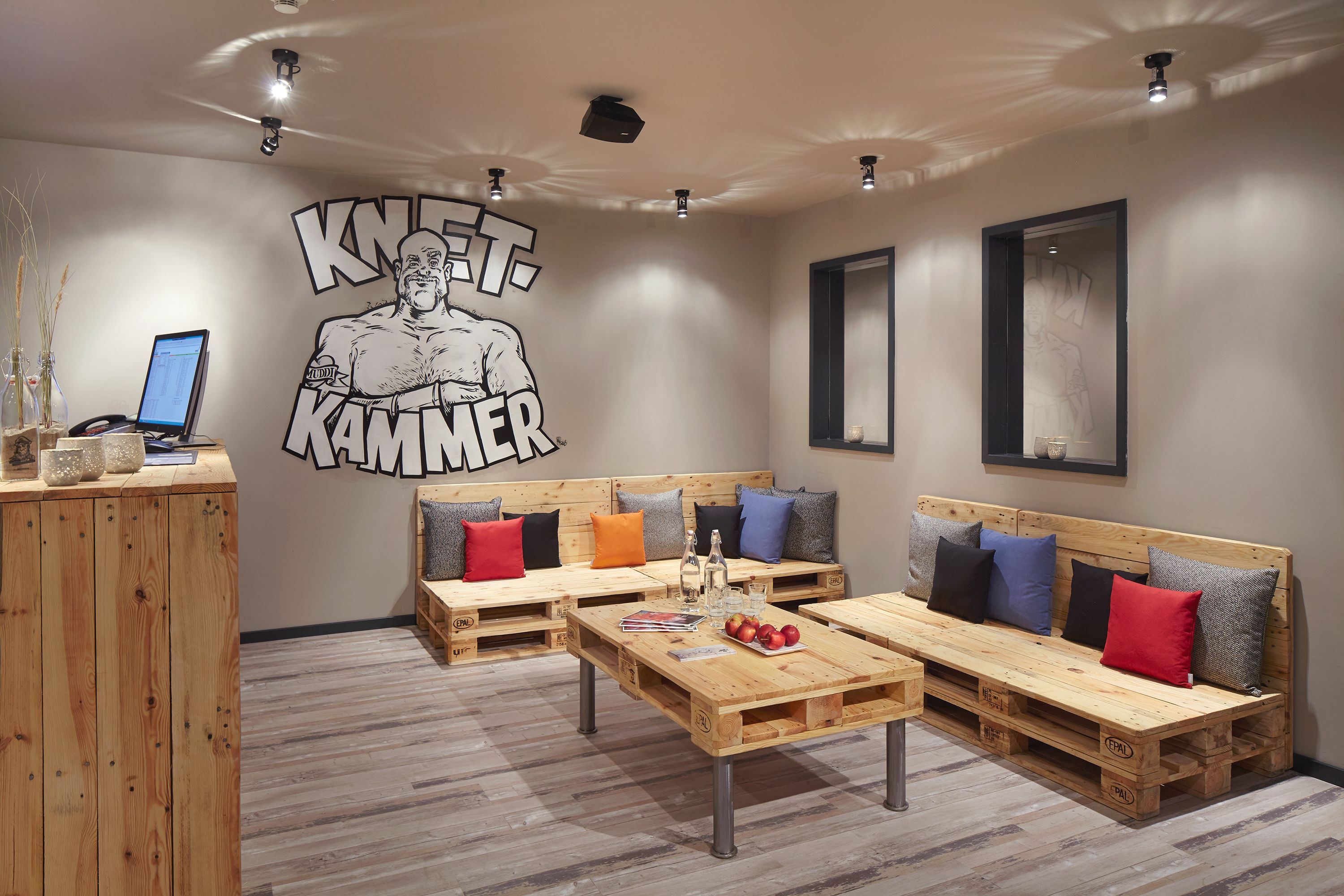 Een moderne lounge met houten meubels, een groot muurdecor en een computer op een bureau.