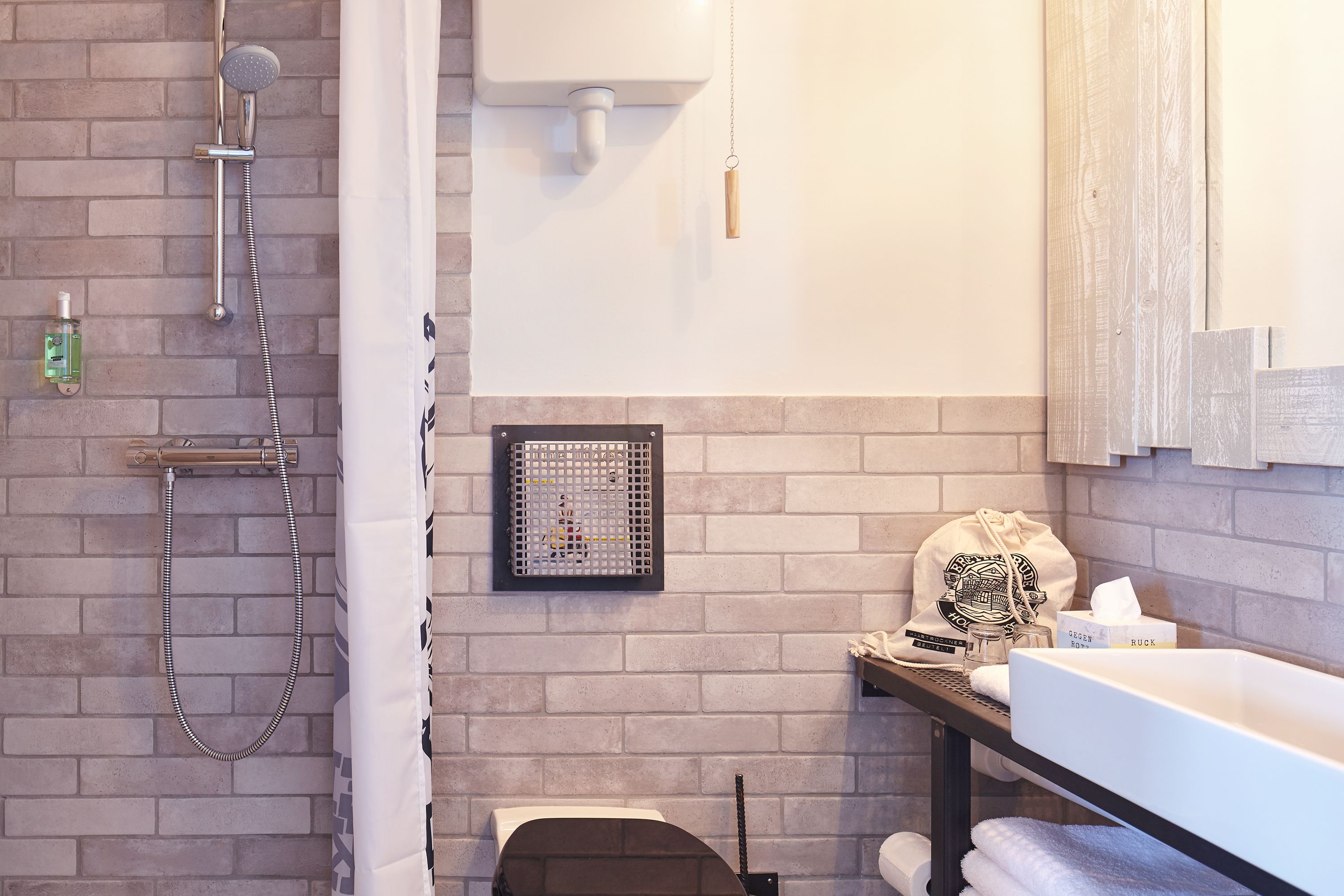 A bathroom with a shower, a toilet, and a sink. There is a towel rack and a small shelf with toiletries.