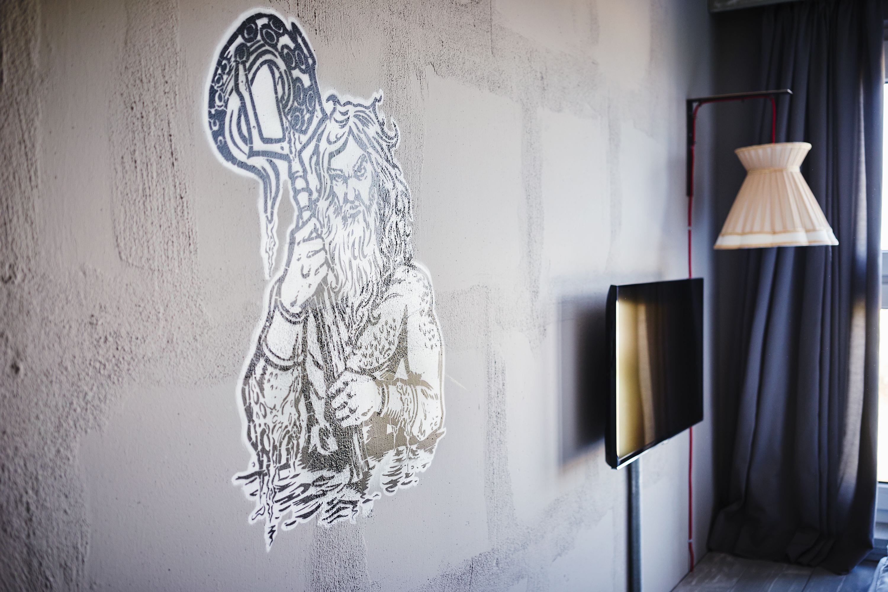 Eine Wand mit einem großen, monochromen Wandgemälde einer Figur, die eine Stange hält. Ein Flachbildfernseher ist rechts an der Wand befestigt.