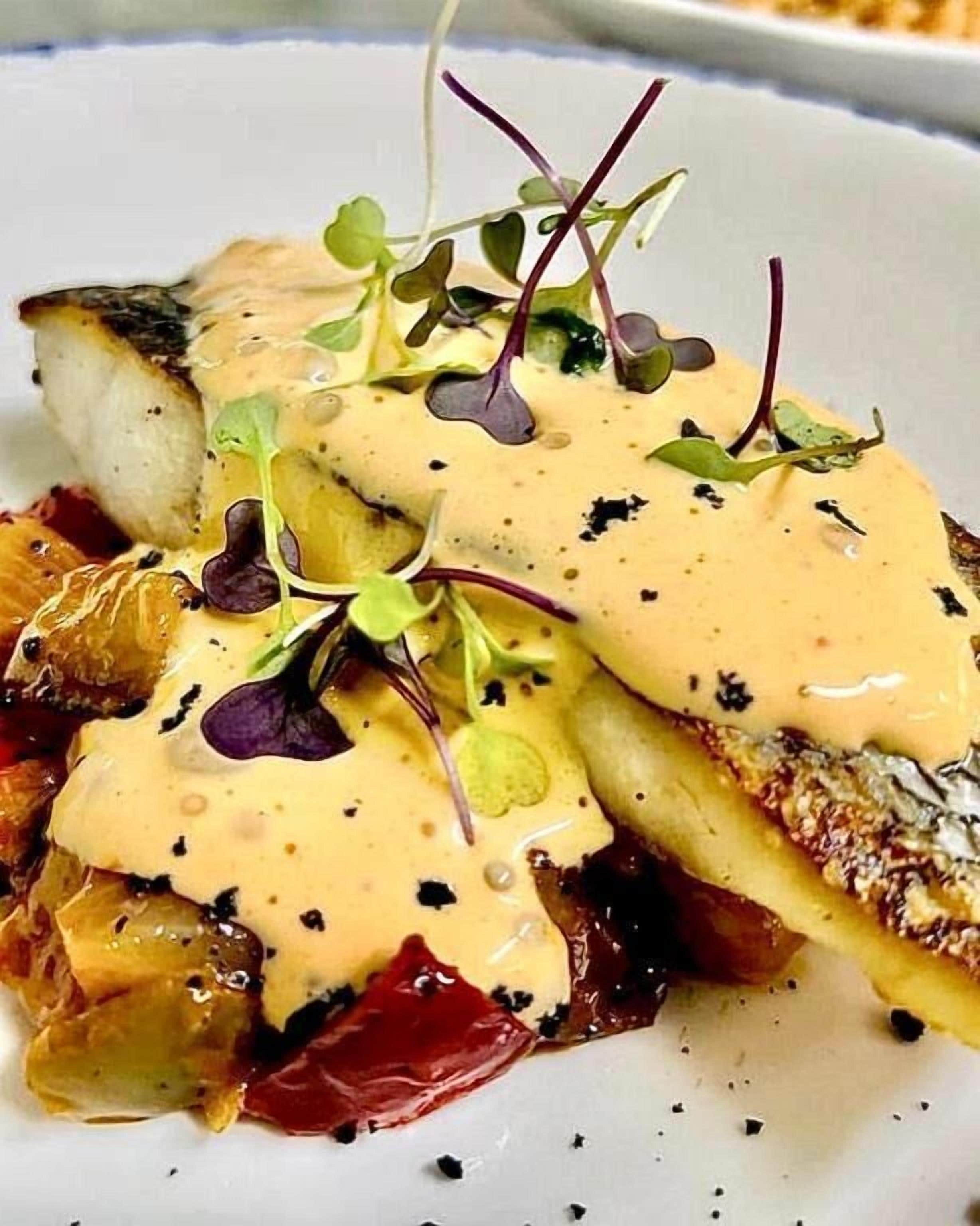 Un plato con pescado, salsa y vegetales verdes.