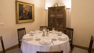 A dining room with a round table set for four, surrounded by wooden chairs. A cabinet with glass doors is visible in the background.