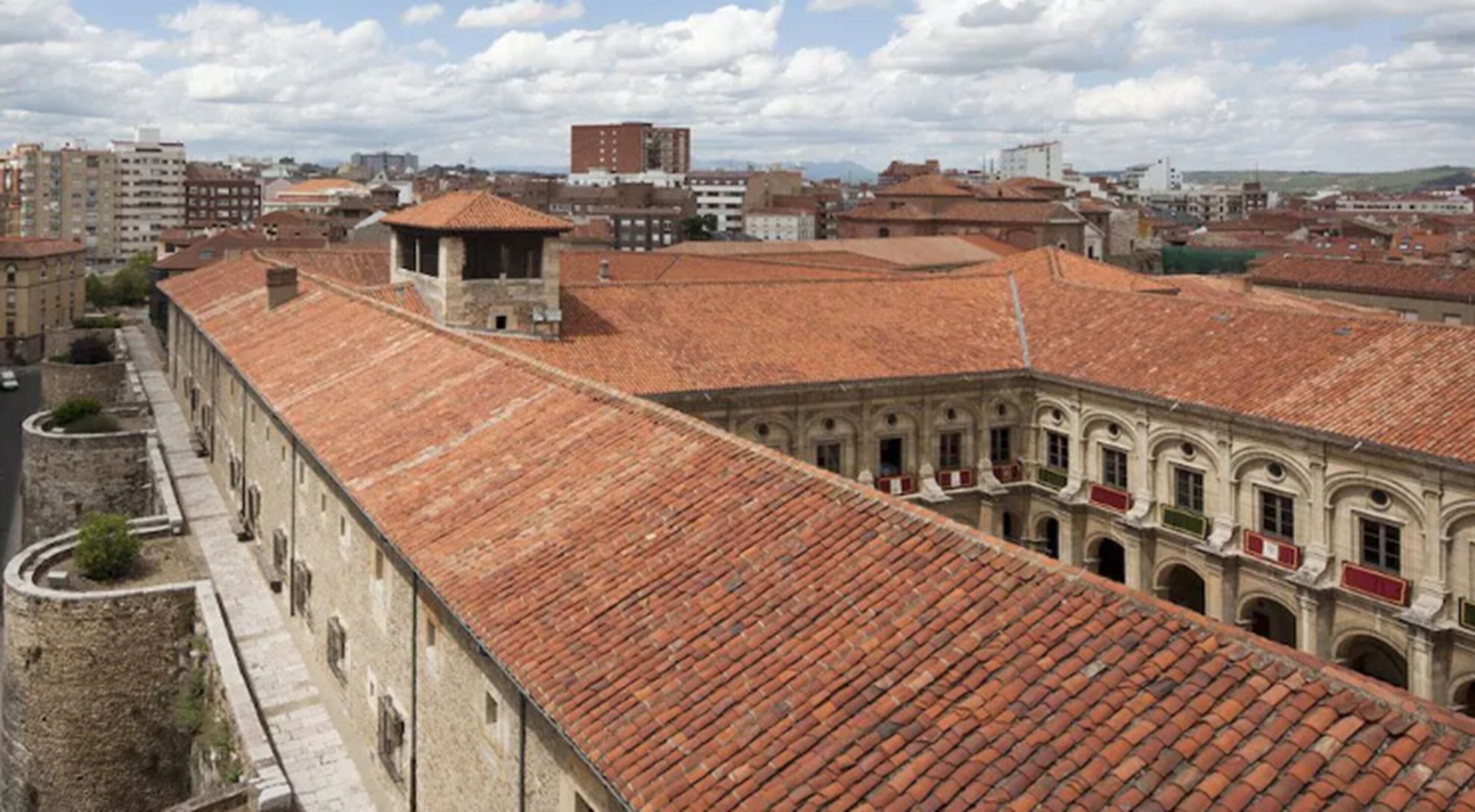 A courtyard with red-tiled roofs and stone buildings, surrounded by a cityscape.