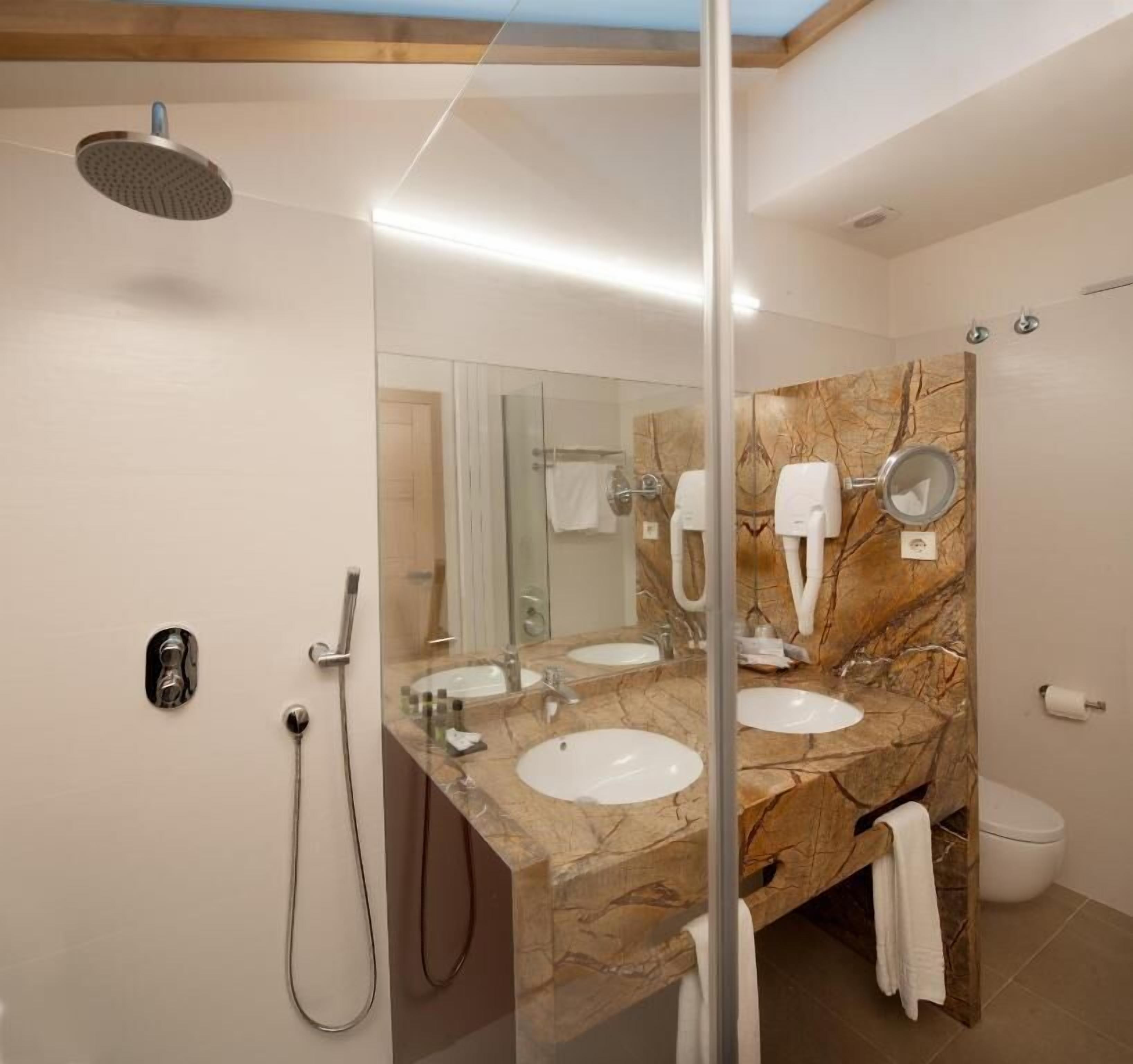 Un baño moderno con dos lavamanos, cabina de ducha de vidrio y encimera de mármol.