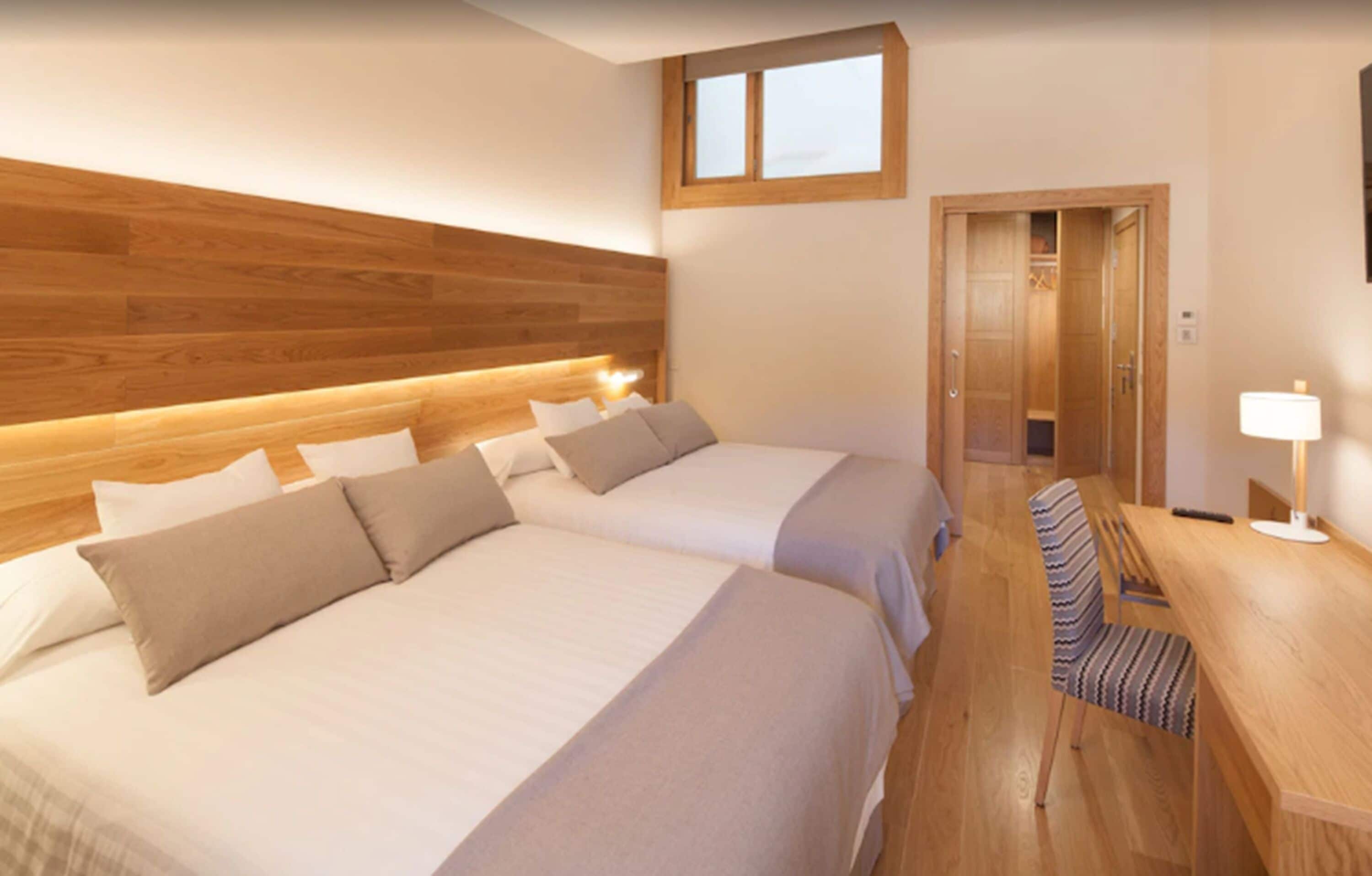 Een hotelkamer met twee bedden, een houten hoofdeinde, een bureau met een stoel en een raam.