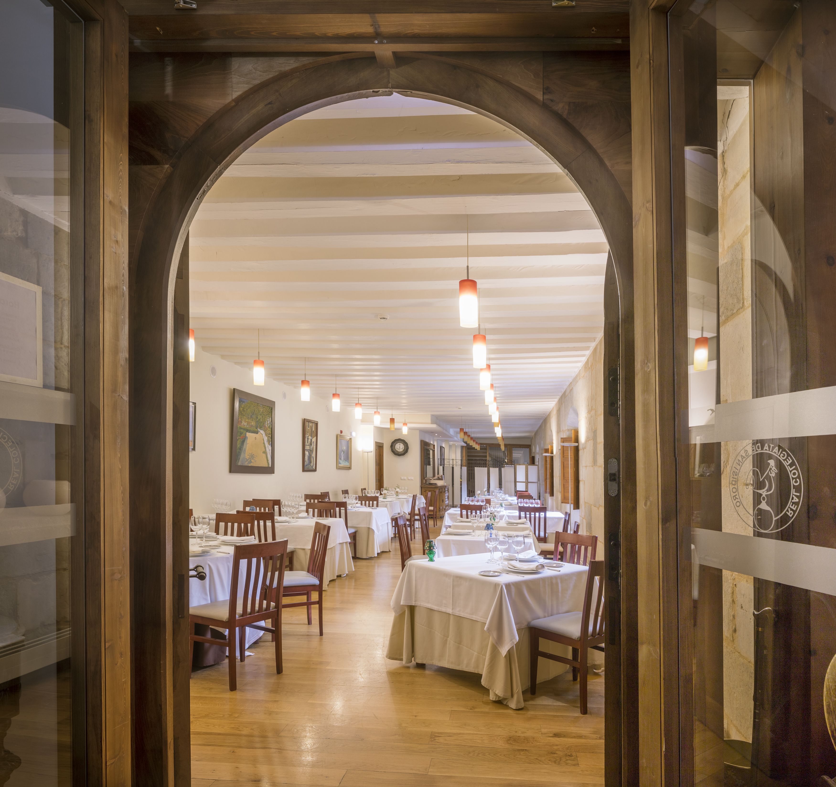 Un restaurant avec des poutres en bois, des tables blanches et des lampes suspendues.